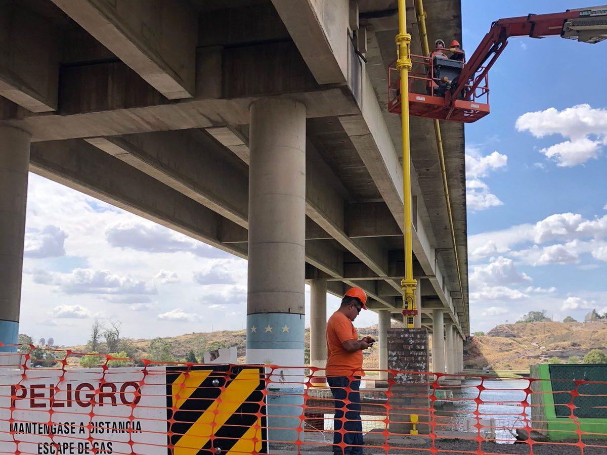 Plataforma elevadora trabajando bajo el puente, con vallado y cartel de escape de gas
